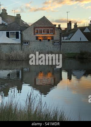 Der Plough Inn Pub und andere alte Steingebäude mit Reflexionen in einem Teich im Dorf Rottingdean, East Sussex, England. Stockfoto