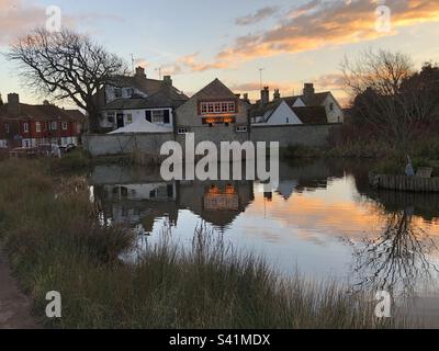 Der Plough Inn Pub und andere alte Steingebäude mit Reflexionen in einem Teich im Dorf Rottingdean, East Sussex, England. Stockfoto