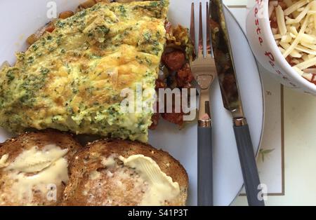 Omelette gefüllt mit Chorizo, Pilzen, Zwiebeln und Käse. Toast und gebackene Bohnen, garniert mit geriebenem Käse an der Seite. Stockfoto