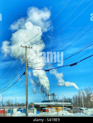 Hemlock-Schild auf einem Gebäude vor einem Kraftwerk, wo Rauch aus Schornsteinen aufsteigt Stockfoto