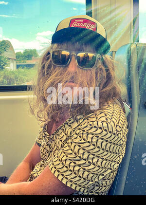 Ein Mann mit langen Haaren und einer Sonnenbrille, der im Zug rummacht Stockfoto