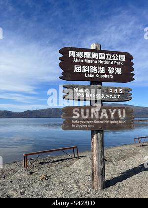 Kussharo-See und hölzernes Hinweisschild. Kawayu, Hokkaido, Japan. 11. November 2022. Japanischer Text (Mittelbrett): Es gibt 477 heiße Spa-Plätze rund um den See Stockfoto