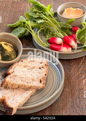 Radieschen und ein Dip auf einem Teller und frisches Brot mit Butter auf einem anderen Tisch Stockfoto