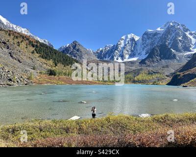 Ein Touristenmädchen am Ufer des Alpensees Shavlinskoye in der Nähe der großen Berge, ein Traum, Märchen, Schönheit im Altai in Sibirien. Stockfoto