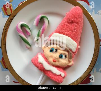 Weihnachtself-Lutscher, der auf ein paar Zuckerstangen auf demselben Teller zu sehen scheint. Bunte festliche Süßigkeiten aus Zucker. Abb. 4. Stockfoto