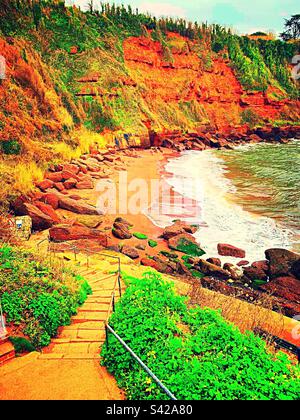 Maidencombe Beach in Torquay ist ein kleiner Sandstrand, der von roten Sandsteinklippen umgeben ist und bei Ebbe interessante Felsenbecken freigelegt sind. Stockfoto