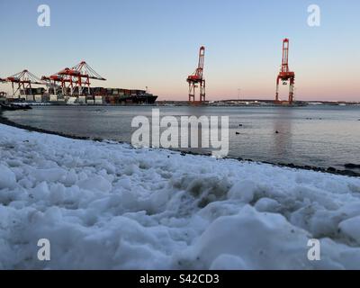 Halifax Seehafen im Winter: Frachtschiffe, die inmitten des geschäftigen Trubels an einem verschneiten Pier anlegen, ein starker Kontrast zu der kalten Luft und schneebedeckten Umgebung. Stockfoto