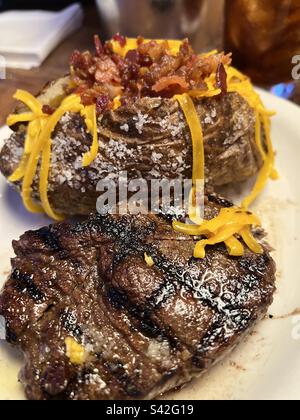 Ein Auftakt eines saftigen, gebratenen, gegrillten Filetsteaks auf einem weißen Essteller mit einer gebackenen Kartoffel gefüllt mit Butter, Speck und gelbem, geriebenem Cheddar-Käse. Texas Roadhouse ein Steakhouse in Texas Stockfoto