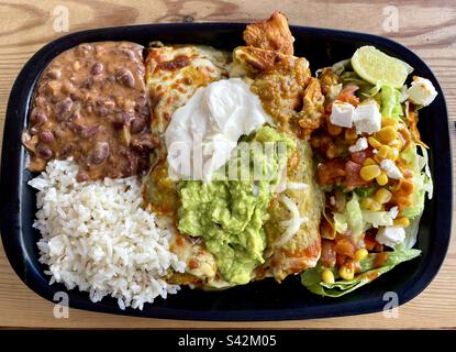 Teller mit Enchiladas Verdes mit Reis, Bohnen und Beilagensalat. Enchiladas werden mit Guacamole und saurer Sahne garniert Stockfoto