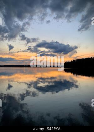 In der finnischen Kajaani-Region während eines arktischen Sommers reflektieren sich brodelnde dunkle Sturmwolken in einem großen See während der Mitternachtssonne Stockfoto