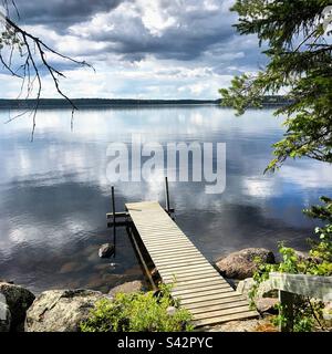 Grüblerische dunkle Sturmwolken spiegeln sich in einem großen See an einem Sommerpier in der Kajaani-Region Finnlands während eines arktischen Sommers Stockfoto