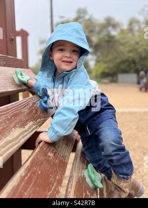 3-jähriger kleiner Junge, der an einem bedeckten Tag auf Spielplatzgeräten in einem Park spielt Stockfoto