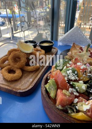 Calamari-Ringe und ein griechischer Salat auf einem blauen Tisch in einem Restaurant Stockfoto