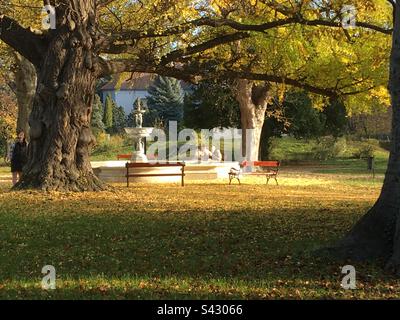 Brunnen und entspannende Menschen sitzen im Herbst auf einer Bank im Park der Lenck-Villa in Sopron, Ungarn Stockfoto