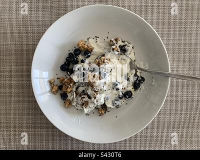 Eine Schüssel mit griechischem Joghurt mit Müsli, Blaubeeren, Chiasamen und Honig vor beigefarbenem Webhintergrund Stockfoto