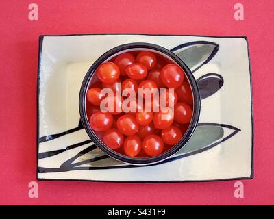 Direkt über dem Blick auf Kirschtomaten in der Schüssel auf dem Teller auf rotem Hintergrund. Stockfoto