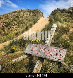 Ein fantasievolles Schild mit der Aufschrift „Leave only Footprints“ auf einem Pfad in den Sanddünen des öffentlichen Strands in Llangennith bei Rhossili in der Region Gower in Westwales Stockfoto