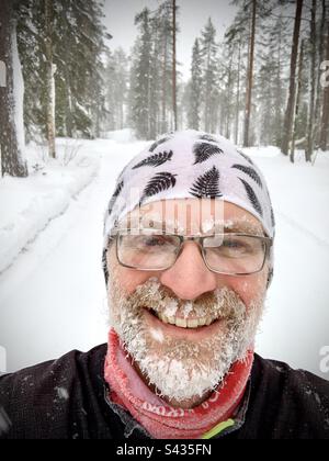 Ein lustiges Selfie eines Mannes mittleren Alters mit Eisbart, der in der extremen Kälte des tiefgefrorenen Winters im nördlichen Polarkreis Finnlands gelaufen ist Stockfoto
