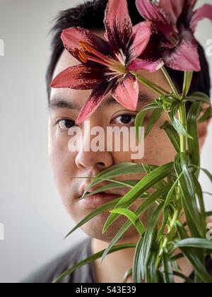 Nahaufnahme eines jungen Asiaten mit roten Lilien auf weißem Hintergrund. Stockfoto