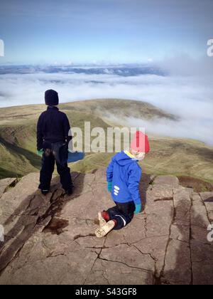 Im Brecon Beacons Bannau Brycheiniog in Wales spielen zwei Kinder auf dem Pen y Fan-Berg über den Wolken. Dies ist der höchste Gipfel im südlichen Teil des Vereinigten Königreichs. Stockfoto