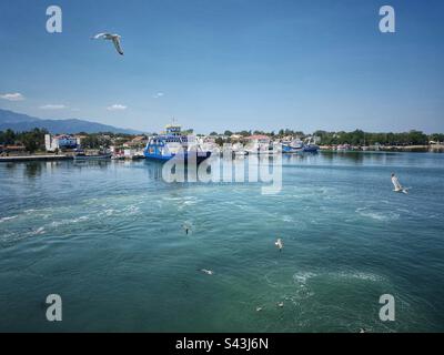 Blick auf den Hafen vom Meer mit Fähre und fliegenden Möwen in Keramoti in Griechenland. Stockfoto