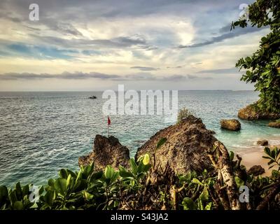 Malerischer Blick auf felsigen Strand, Meer, Boot und Himmel in Jimbaran, Bali, Indonesien. Stockfoto