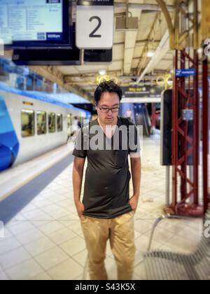 Ein junger asiatischer Mann mit Brille steht am Bahnhofsplatz in Melbourne, Victoria, Australien, selektiver Fokus. Stockfoto
