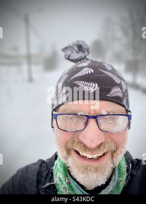 Ein lustiges Selfie eines Mannes mittleren Alters mit gedämpften Gläsern, die mit Graupel und Eisbart bedeckt sind, nachdem er im Winter in Finnland in einem Schneesturm gelaufen ist Stockfoto