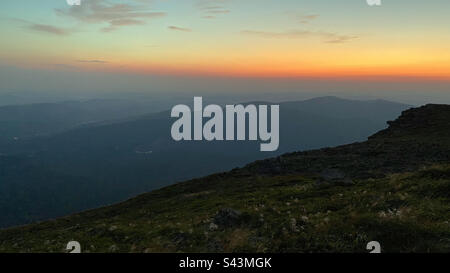 Berge bei Sonnenaufgang. Natürliche Berglandschaft mit beleuchteten nebligen Gipfeln, nebligen Hängen und Tälern, blauer Himmel mit orangefarbenem gelbem Sonnenlicht. Fantastische Szene von Beskid Zywiecki in Polen Stockfoto