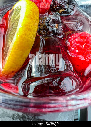 Ein Glas schwarzen Johannisbeeren-Gin mit Beeren und Zitrone Stockfoto
