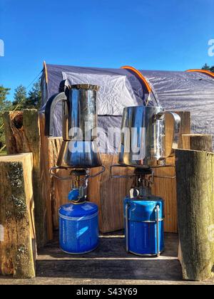Zubereitung von Kaffee auf einem Campingherd im Freien in einem Mokakopf mit Baumstämmen als Windschutzscheibe Stockfoto
