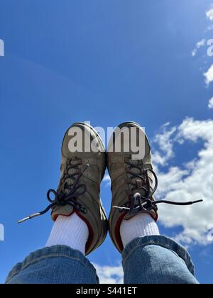 Füße hoch in die Luft. Beigefarbene Wanderschuhe, weiße Socken und die Unterseite blauer Jeans mit blauem Himmel. Stockfoto