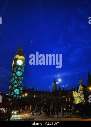 Der Mond erhebt sich über einem beleuchteten Parlamentsgebäude in London - beleuchtet mit Bildern von Blumen, die Länder des Vereinigten Königreichs zur Krönung von König Karl III. Repräsentieren Stockfoto