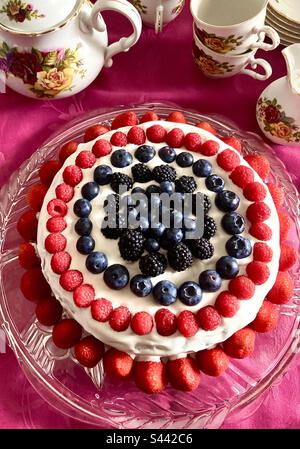 Hausgemachter Schwammkuchen mit Schlagsahne, Erdbeeren, Heidelbeeren, Himbeeren und Brombeeren mit Nachmittagstee Victoria & Albert Teekanne und Tassen und Untertassen Stockfoto