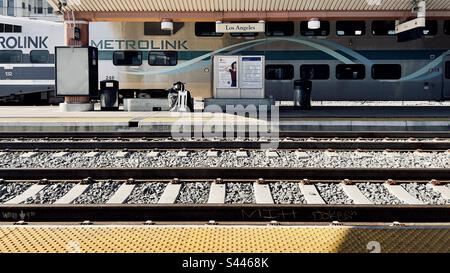 LOS ANGELES, CA, 2022. DEZ.: Anonyme Person, die mit dem Koffer auf dem Bahnsteig in der Union Station in Downtown auf den Boden blickt, mit dem Metrolink-Zug dahinter Stockfoto