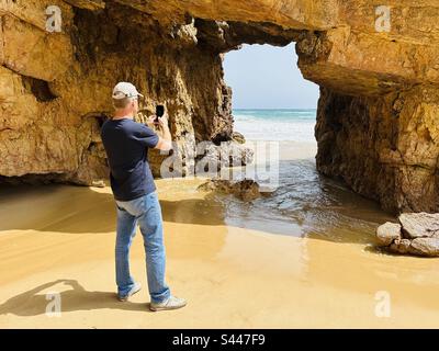 Touristen fotografieren eine natürliche Felsformation am Strand Praia das Furnas an der Algarve Stockfoto