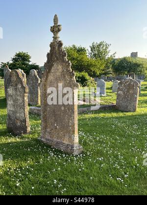 Wunderschöne Grabsteine aus Granit an den Gräbern der Nikolaikirche inmitten von Gras und Gänseblümchen an einem Sommerabend mit Katharinenkapelle im Hintergrund, Abbotsbury, Dorset, vereinigtes königreich Stockfoto