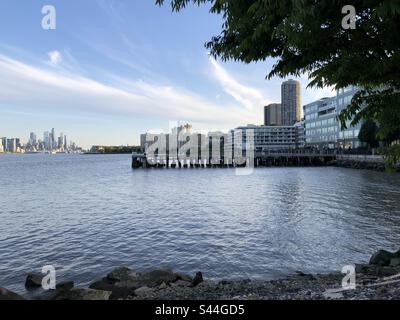 Dieses fesselnde Foto zeigt ein malerisches Leben am Wasser. Das Bild zeigt das Flussufer mit einem gepflegten Gehweg, der in ein modernes Apartmentgebäude führt, das die lebendige Skyline der Stadt definiert Stockfoto