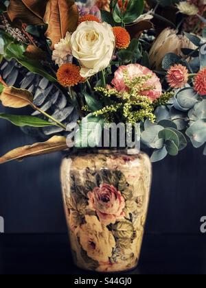 Nahaufnahme eines Blumenstraußes mit frischen Blumen und Blättern in einer Vase mit Blumenmuster im Vintage-Design auf schwarzem Hintergrund. Vintage-Style. Kunst Stockfoto