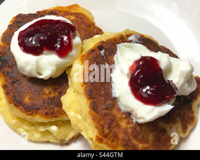 Zwei ukrainische Syrniki (Käsepfannkuchen) werden auf traditionelle Weise mit Sauerrahm und Marmelade serviert. Stockfoto