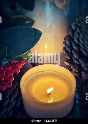 Blick aus einem hohen Winkel auf die beleuchtete Kerze und die Reflexion in Keramikfiguren, umgeben von Cotoneaster-Beeren und Pinienzapfen. Vintage-Style. Herbst-/Weihnachtsthemen. Spiritualität. Feier. Dekoration. Stockfoto