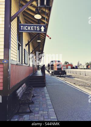 Altmodisches Bahnhofsgebäude mit einem Schild mit der Aufschrift Tickets und einer alten Lokomotive, die auf Gleisen am Touristenort Essex Steam Train in Essex, Connecticut, USA, geparkt ist Stockfoto