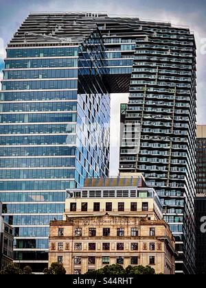 Nebeneinander. Collins Arch, ein moderner Wolkenkratzer, zwei Türme, die durch eine mehrstöckige Skybridge miteinander verbunden sind, ragt über ein denkmalgeschütztes Gebäude im Geschäftsviertel von Melbourne, Victoria, Australien. Alt gegen neu. Stockfoto