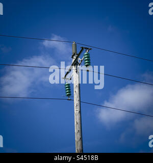 Hölzerne Strommasten mit Glasisolatoren zwischen den Kabeln. UK Stockfoto