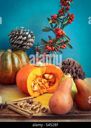 Stilleben von Kürbissen, Pinienzapfen, Birnen, Walnüssen, Gewürzen und Orangenbeerzweigen vor blauem Hintergrund. Herbstthema. Feier. Dekor. Stockfoto