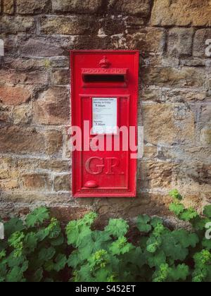 Ein alter roter Briefkasten in einer Steinwand mit den Buchstaben GR für König George V. das weiße Informationsblatt zeigt an, dass es sich um einen aktiven Briefkasten mit einer täglichen Royal Mail-Abholung handelt. Stockfoto