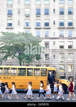 Schulkinder laufen vor einem geparkten gelben Bus Stockfoto