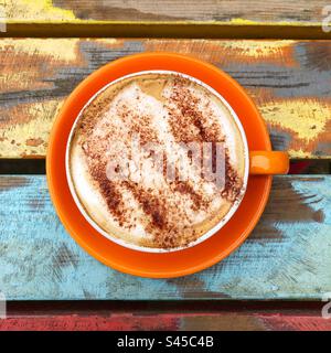 Heißgetränke, Speisen, die in einer bunten Tasse und Untertasse mit einem schaumigen Cappuccino-Kaffee und Schokoladenstreuseln serviert werden Stockfoto