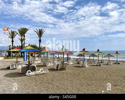 Farbenfrohe Sonnenschirme und Sonnenliegen stehen im Frühsommer in Sabinillas im Süden Spaniens zur Verfügung Stockfoto