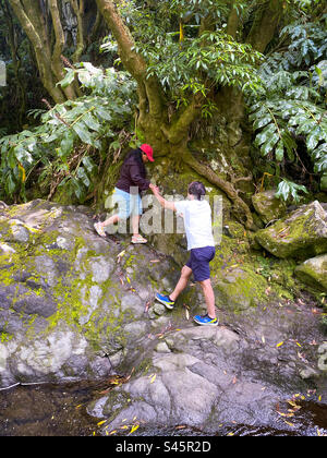 Der Wanderführer hilft einer Frau beim Navigieren in felsigem Gelände in einem tropischen Wald auf Sao Miguel Island, Azoren, Portugal Stockfoto